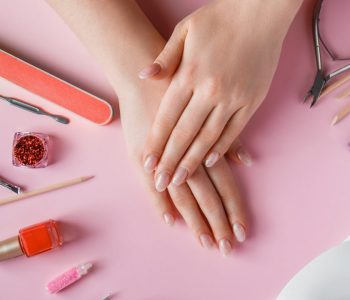 nail-care-procedure-in-a-beauty-salon-female-hands-and-tools-for-manicure-on-a-pink-background-